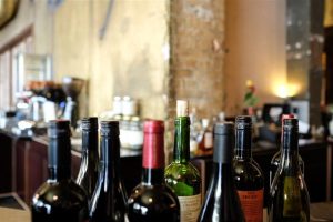Home Online wijn kopen: verschillende wijnflessen op tafel bij een glas wijn, illustrerend hoe makkelijk het thuis bestellen is.